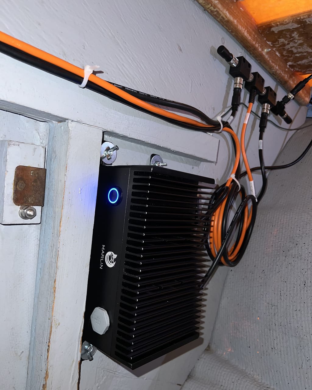 A Marlin box mounted on a bulkhead aboard a boat, powered on with its blue status ring lit